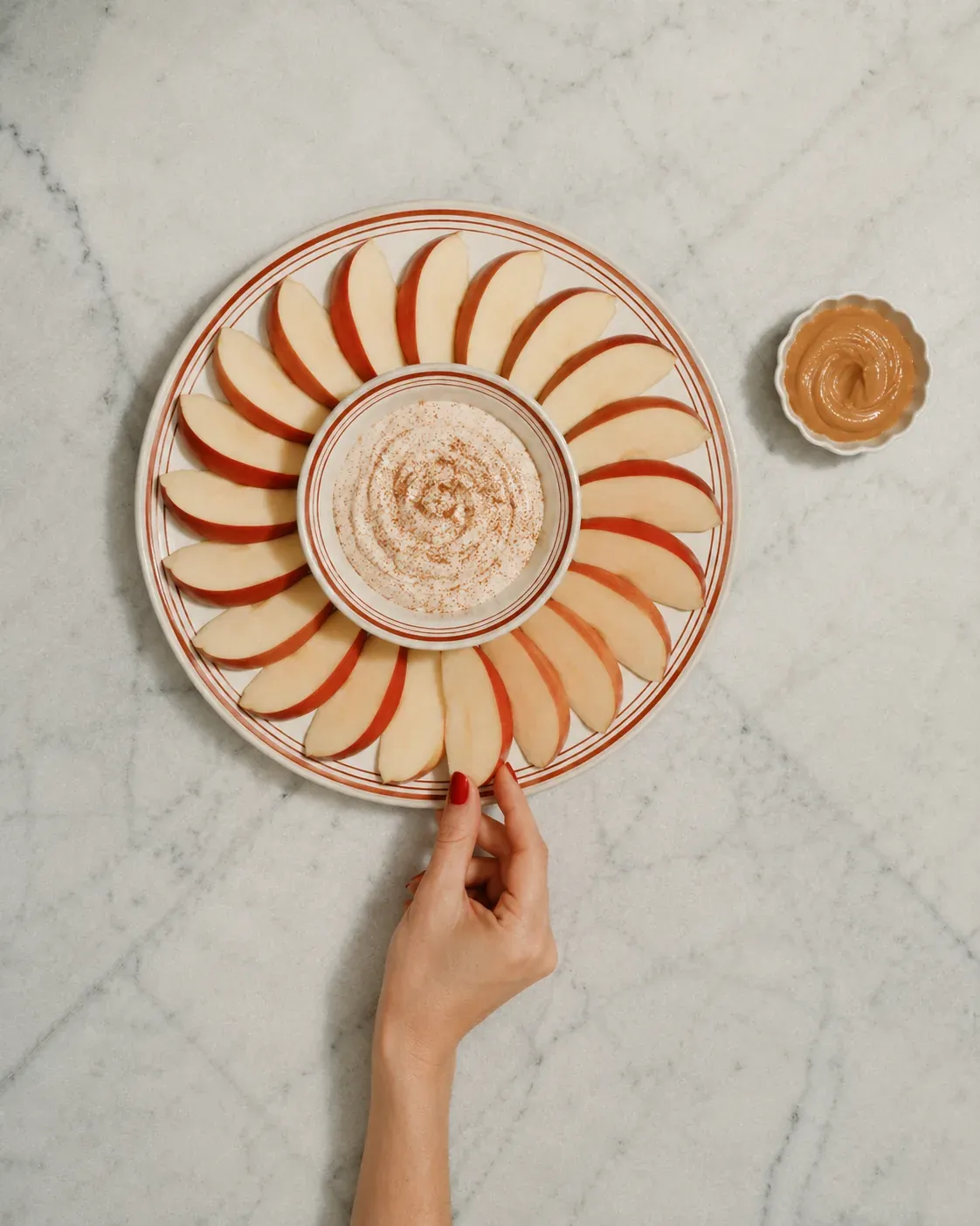 Sliced apple with Greek yogurt, cinnamon, and nut butter on a striped plate for a sweet high-protein snack | Becoming Elysian quiet luxury wellness