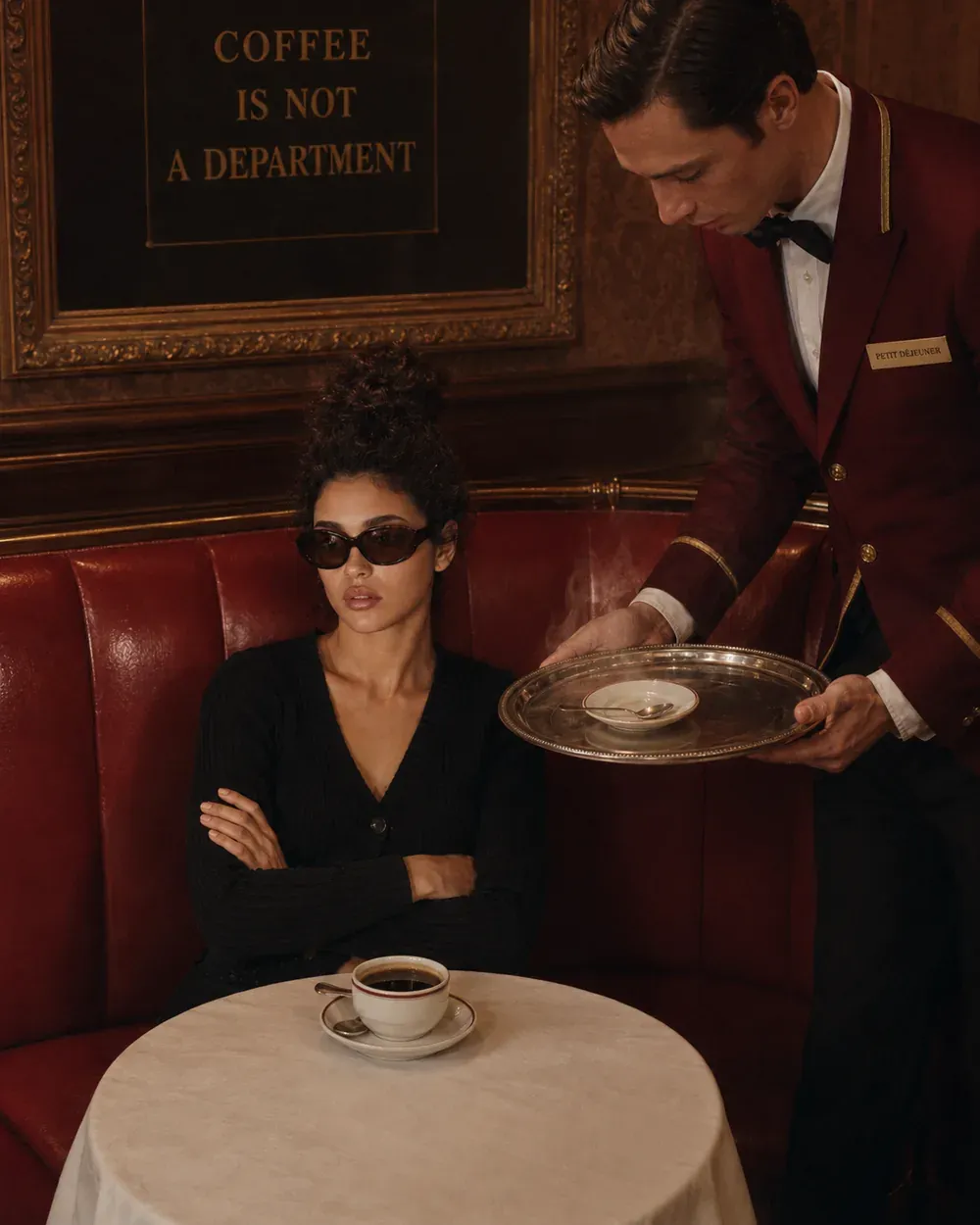 Woman in an old-world cafe as a waiter serves coffee under a sign reading coffee is not a department