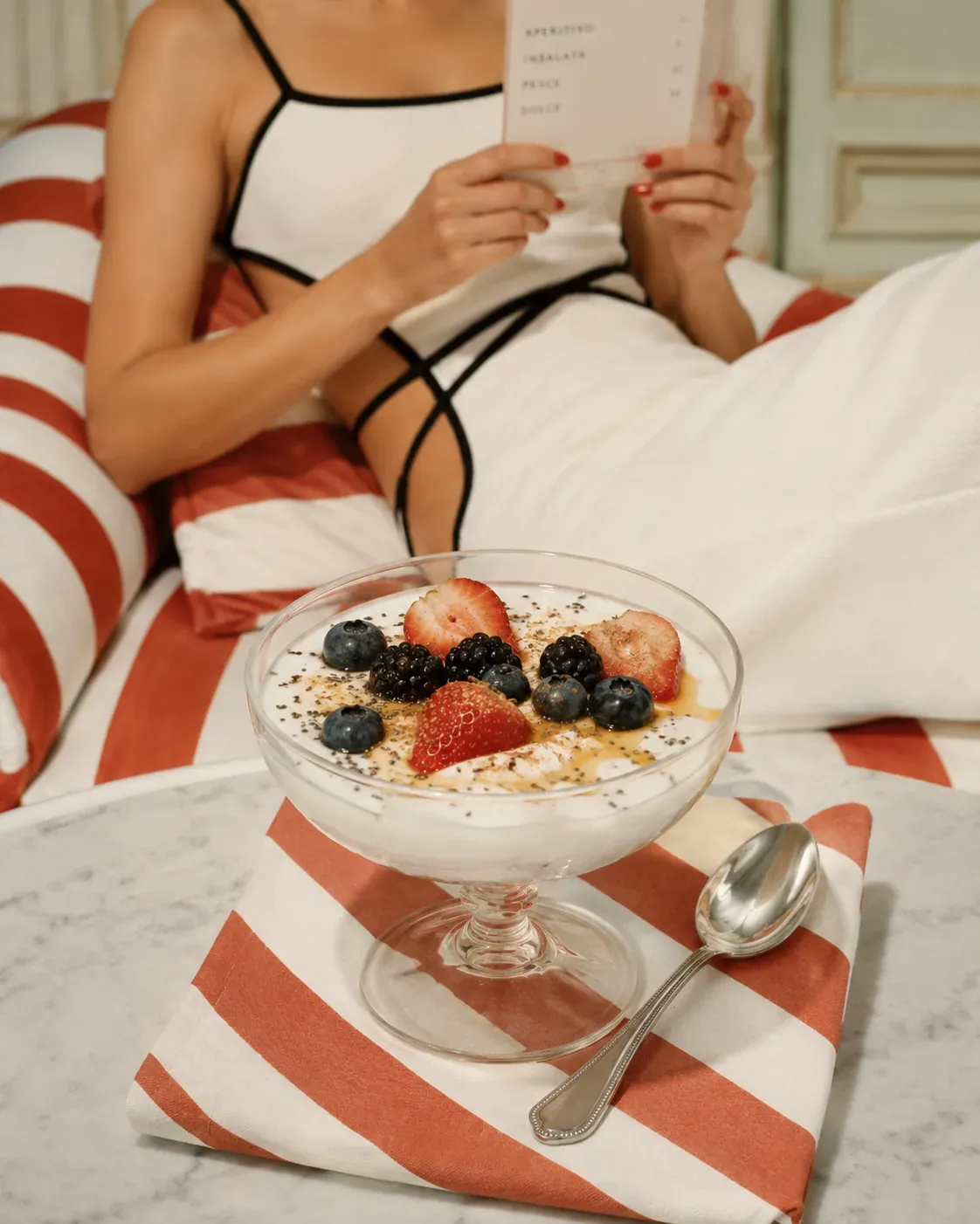 Creamy Greek yogurt snack bowl with berries, chia seeds, cinnamon, and honey in a vintage striped poolside setting | Becoming Elysian quiet luxury wellness
