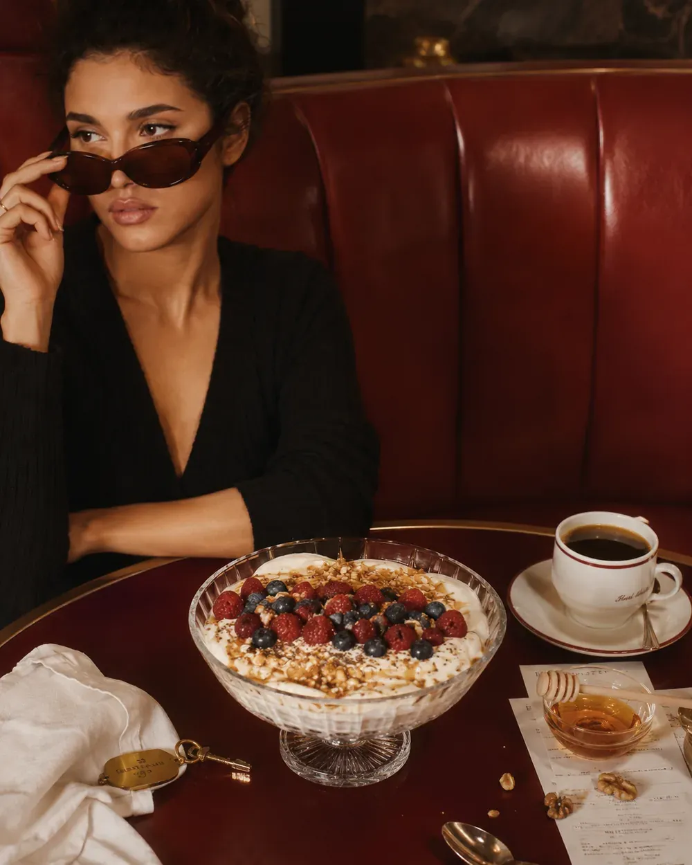 Large yogurt bowl with berries, walnuts, chia seeds, honey, and coffee on a red cafe booth table